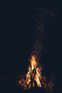 Blazing campfire at night throwing a scattering a sparks into the air like ideas floating from the flame of inspiration and the kindling of writing prompts.