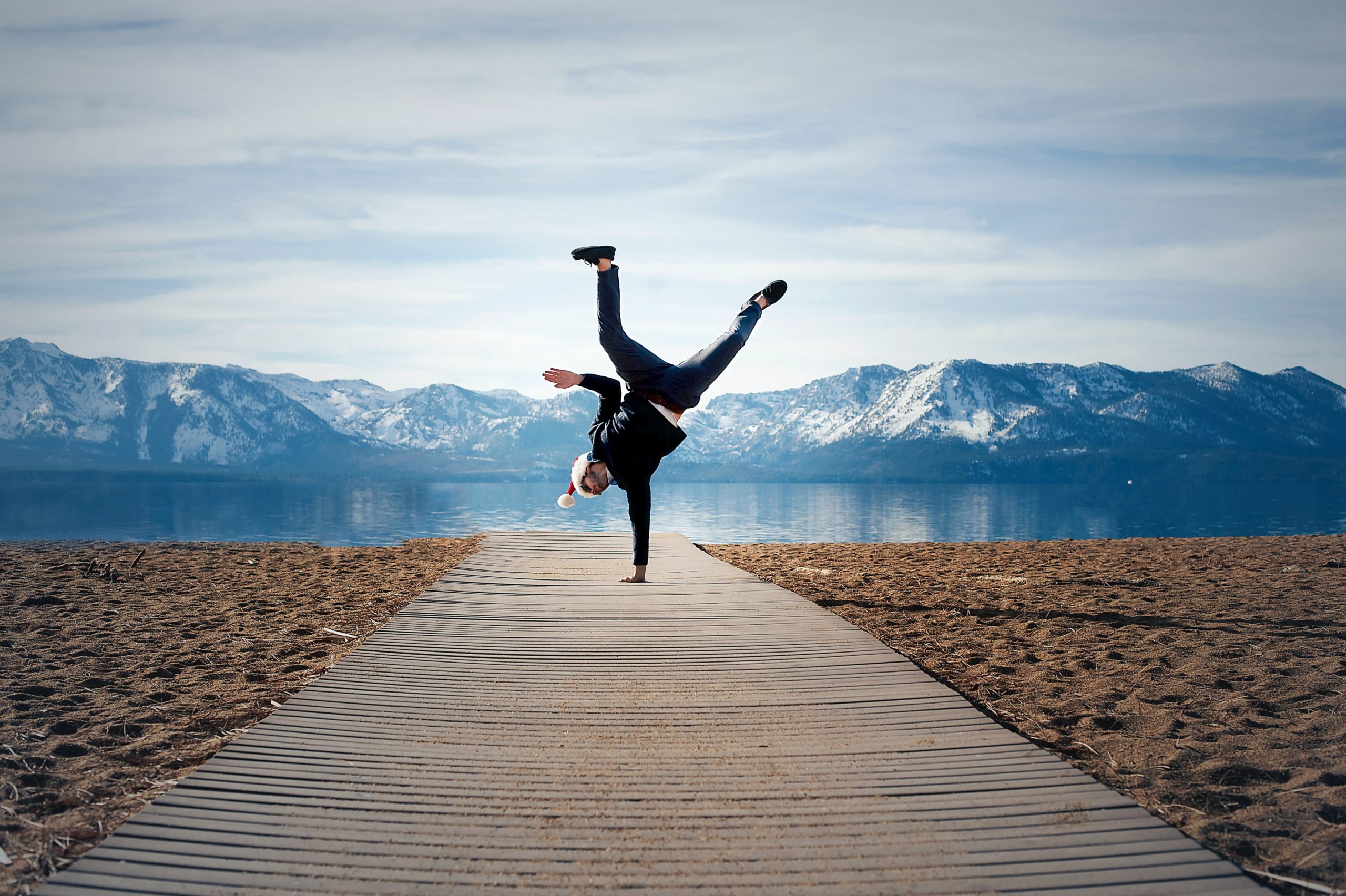 Person showing some creative confidence while doing a one-handed handstand on a dock leading to a blue lake.