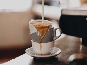 Three precariously stacked mugs with coffee pouring into them and spilling from one to the other—i.e., a visual representation of what happens when life becomes a lot.