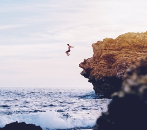 A person demonstrating how to trust your gut by jumping off a cliff into waves the same way writers sometimes have to send things out to get published.