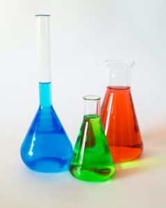 Three glass beakers containing colored water for a scientific experiment involving word count, other writers' process, and figuring out how to write at your own pace.